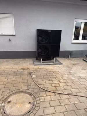 Wärmepumpen-Außengerät auf einer eingefassten Aufstellfläche neben dem Wohnhaus